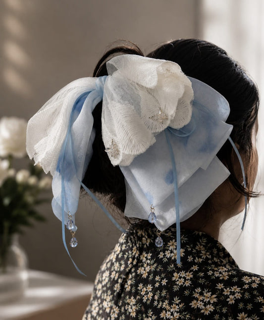 Model wearing a large, oversized handmade hair bow clip featuring layers of light blue sheer fabric and delicate white lace with embroidered details and hanging crystal bead dangles