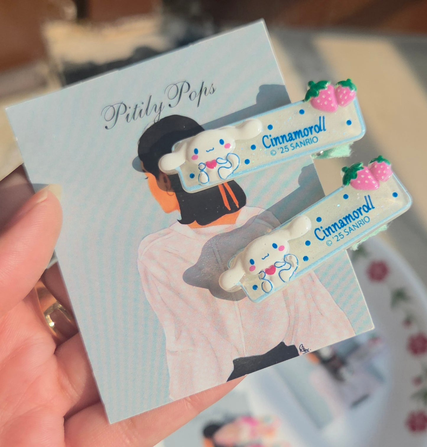 Pair of sky blue and white glittery kids hair clips featuring the flying puppy cartoon character Cinnamoroll with pink fruit accents.