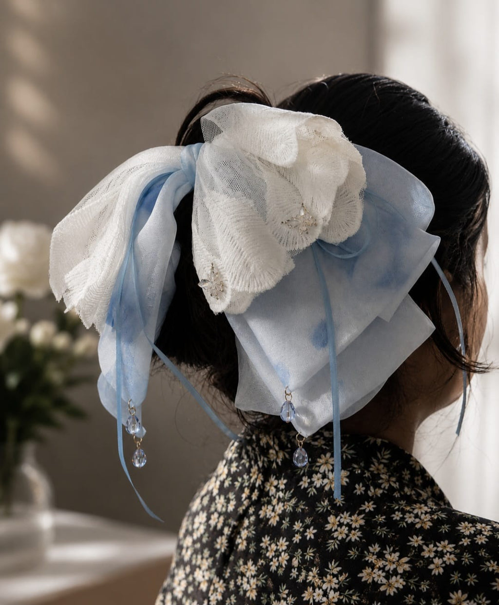 Model wearing a large, oversized handmade hair bow clip featuring layers of light blue sheer fabric and delicate white lace with embroidered details and hanging crystal bead dangles