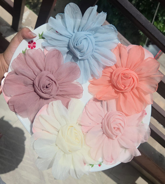    Five oversized chiffon fabric flower hair clips in dusty mauve, sky blue, soft peach, cream white, and pastel pink on a plate.
