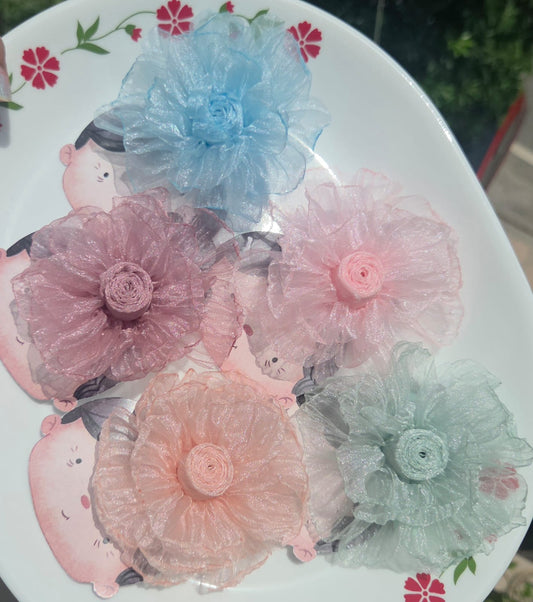 Five sheer organza flower hair clips in pastel blue, dusty mauve, blush pink, peach cream, and sage mint displayed on a decorative white plate.