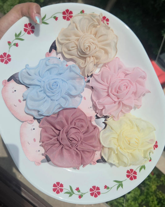 Five colorful fabric rosette flower hair clips with alligator backs arranged on a decorative plate, featuring cream, blue, pink, dusty rose, and yellow colors.