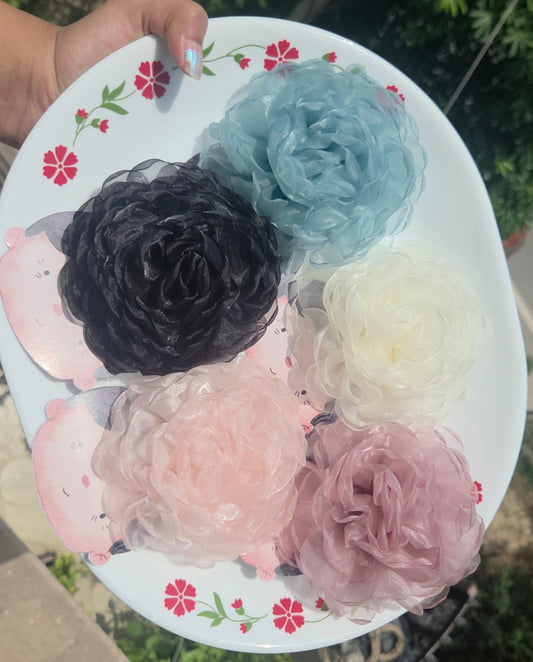 Five colorful large organza flower hair clips with alligator clip backs displayed on a white plate.