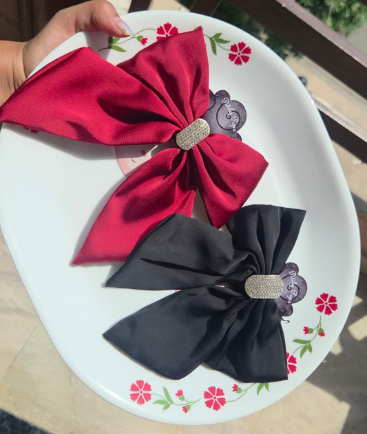 ​Elegant red and black satin hair bows with sparkling crystal centerpieces and alligator clips on a decorative plate.