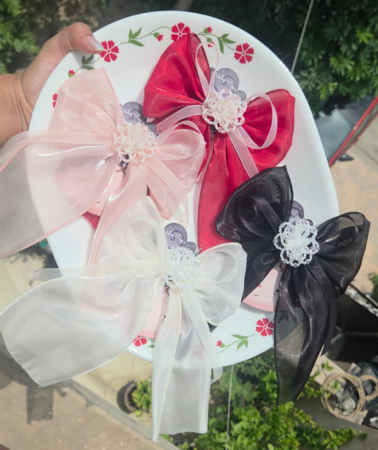 A collection of four large, handmade organza flower hair clips in black, pastel pink, sky blue, and white, arranged on a decorative floral plate.