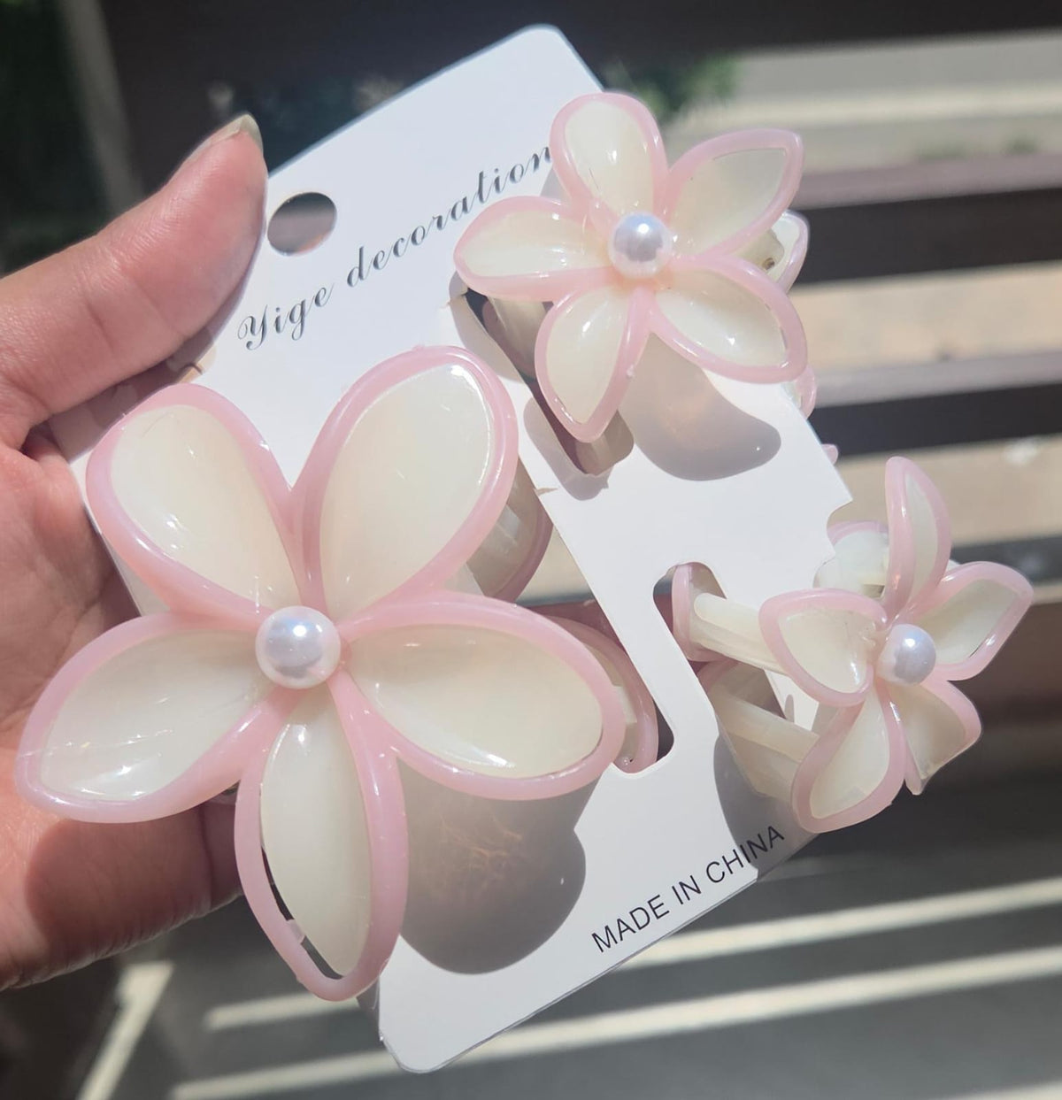 A 3-piece floral hair clutcher set with 1 large and 2 small plumeria claw clips in soft cream with a delicate pink border and faux pearl centers.