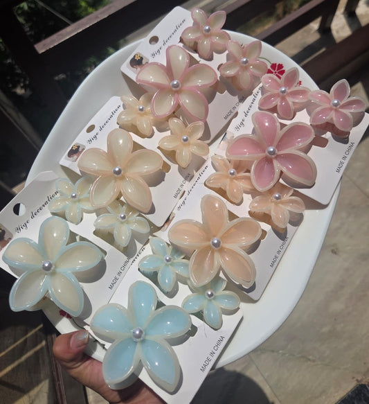 A collection of six 3-piece plumeria flower hair clutcher sets in shades of mint blue, sky blue, light pink, dark pink, peach, and vanilla cream displayed on a white plate.