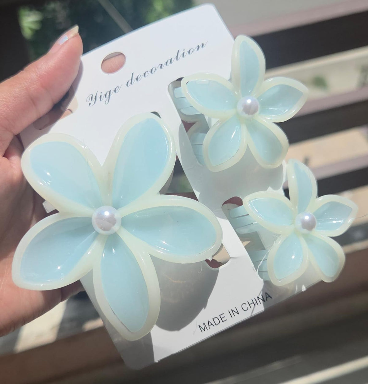 A 3-piece tropical flower claw clip set showing 1 big and 2 small plumeria hair clutchers in a translucent sky blue color with white borders.
