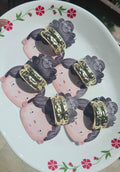 A collection of handmade metallic gold cuff scrunchies with a textured hammered finish displayed on a white floral plate.