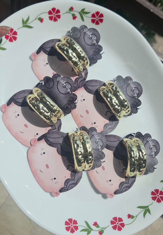 A collection of handmade metallic gold cuff scrunchies with a textured hammered finish displayed on a white floral plate.