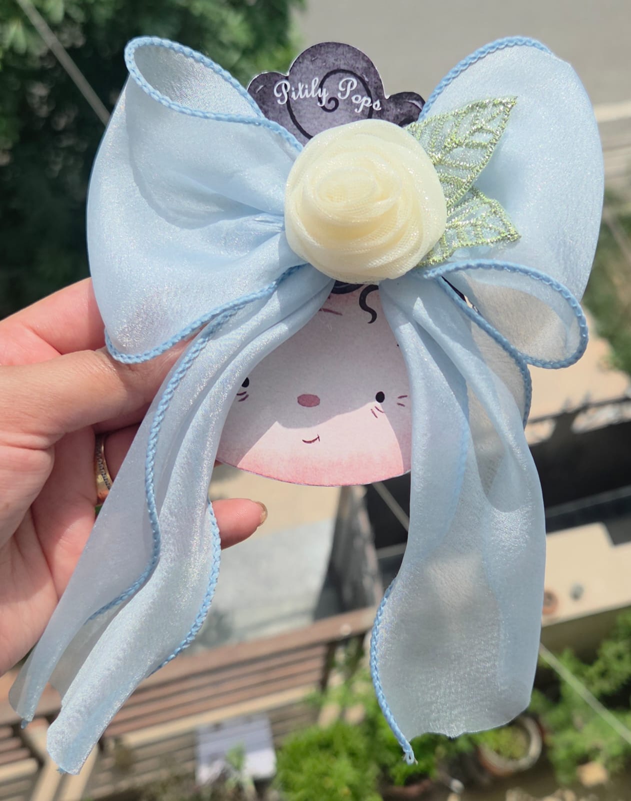 Light sky blue sheer hair bow with a central cream rose accent and leaf detail on an alligator clip.