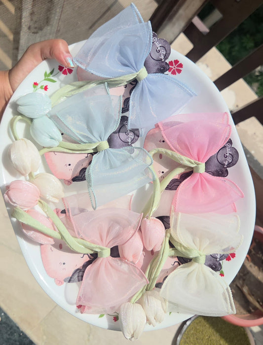 Five pastel organza sheer hair bows with handmade fabric tulip accents arranged on a white decorative plate, showing color variations in blue, mint green, white, and pink.