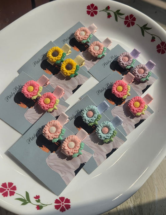    Five pairs of handmade sunflower and daisy kids hair clips in yellow, pink, lavender, and blue displayed on Pitily Pops backing cards.
