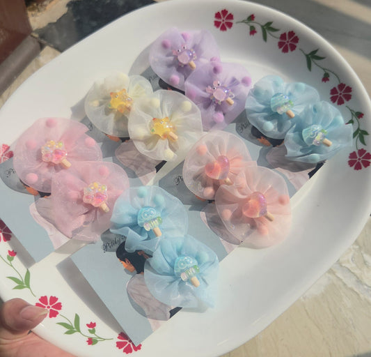 A collection of cute organza tulle kids hair clips sold in pairs on display cards, showing 5 pastel colors including pink, purple, blue, white, and peach with miniature popsicle charms and pom-poms inside.
