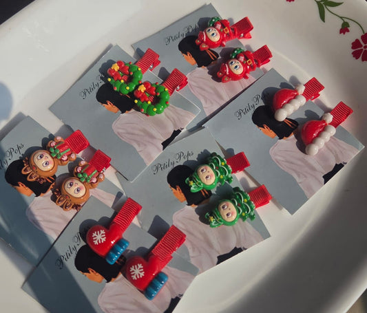 Six pairs of kids Christmas hair clips by Pitily Pops, featuring holiday designs like Santa hats, Christmas trees, wreaths, and mittens on grey display cards.