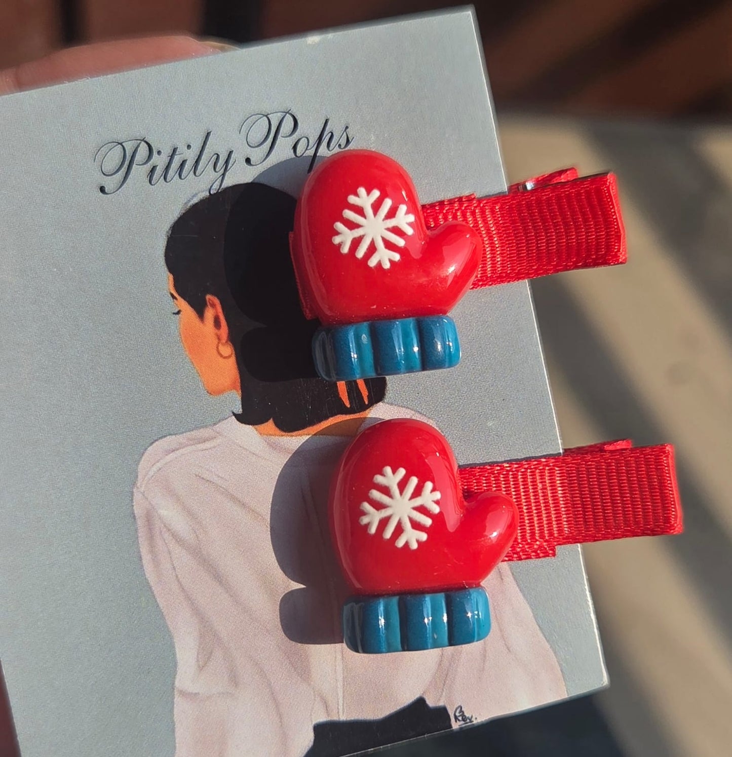 Close-up of winter-themed kids hair barrettes showing festive red elf dolls, gingerbread characters, and snowflake mittens sold as matching pairs.