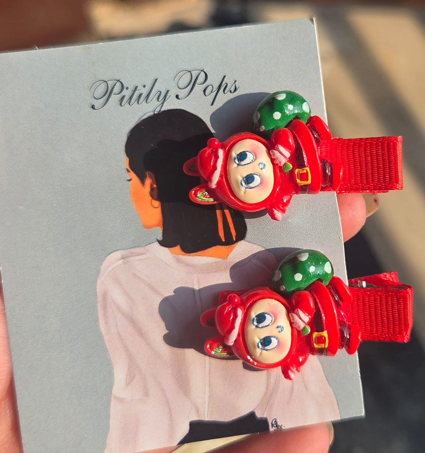 Assorted children's Christmas hair clips including red mittens with snowflakes, green holiday wreaths, decorated Christmas trees, and mini Santa hats.