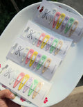 Assortment of colorful pastel snap hair clips arranged on white display cards, held by hand