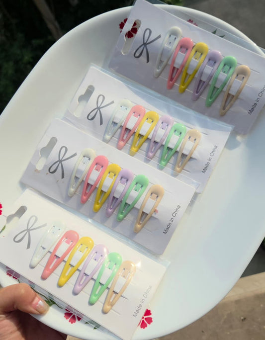 Assortment of colorful pastel snap hair clips arranged on white display cards, held by hand