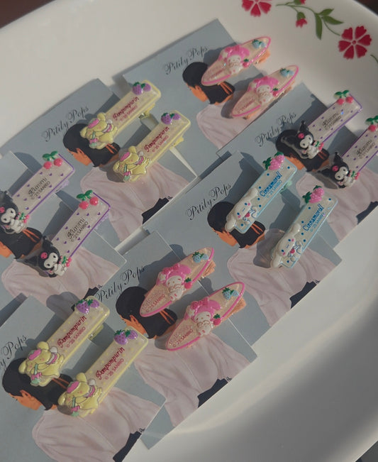 A collection of Pitily Pops kids cartoon character hair clips displayed in pairs on branded backing cards, featuring pastel yellow, pink, purple, and blue designs.