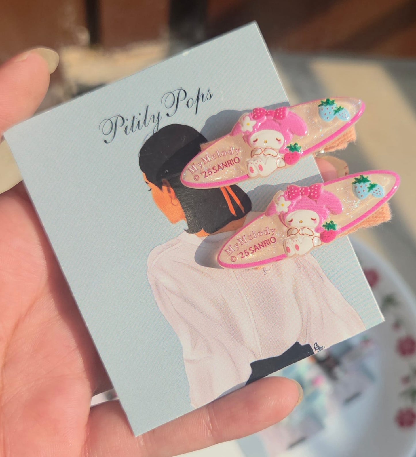 Pair of soft pink girls hair clips featuring the popular cartoon character My Melody decorated with small green and blue berry accents.