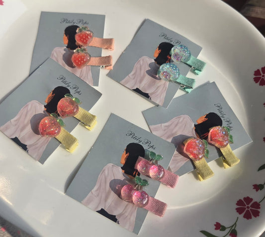 Pair of handmade glitter fruit hair clips for girls in strawberry, cherry, peach, and jellyfish designs by Pitily Pops.