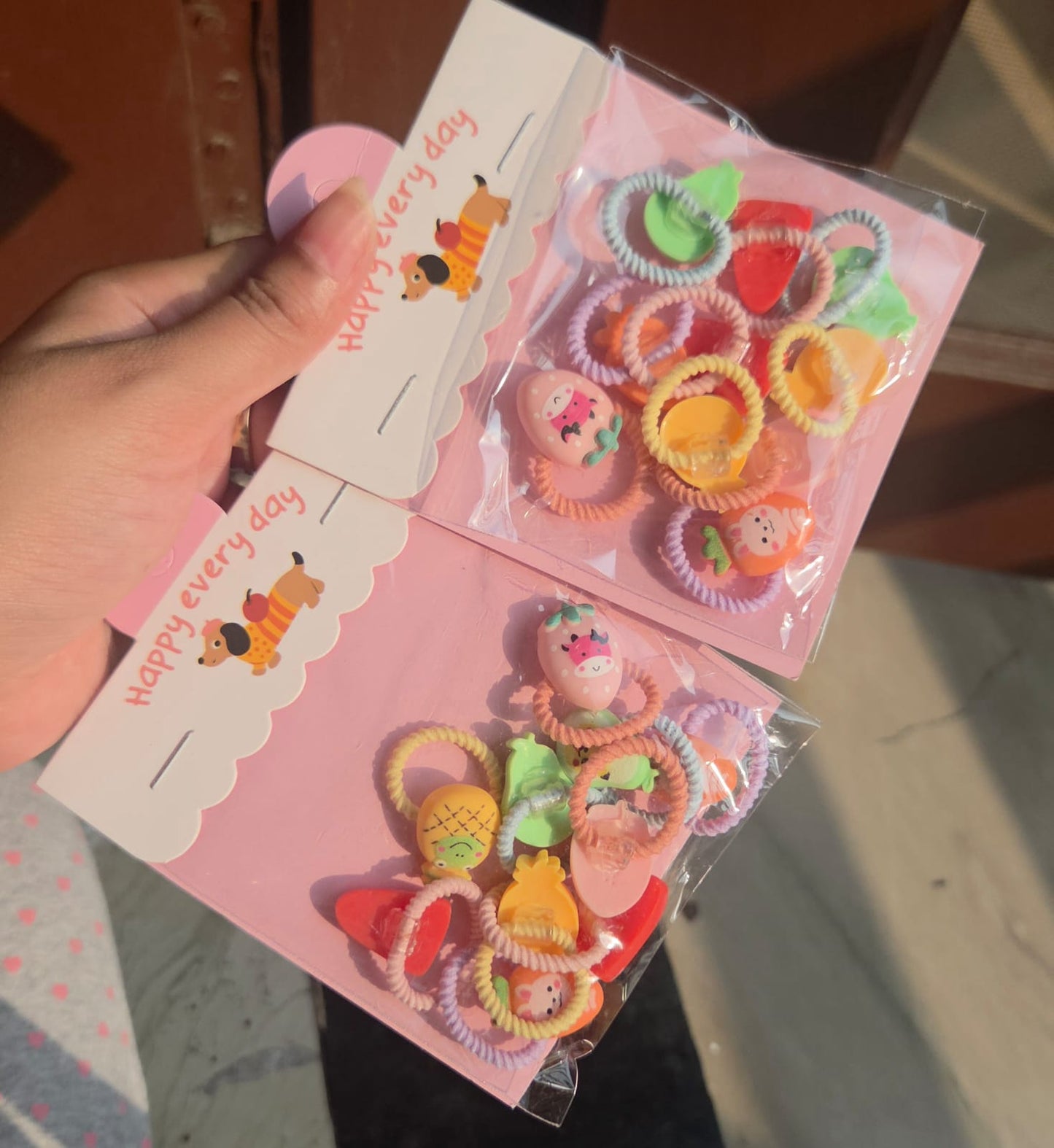 Pack of 5 pairs of colorful kids hair ties in pink Happy Every Day packaging featuring cute fruit charms.