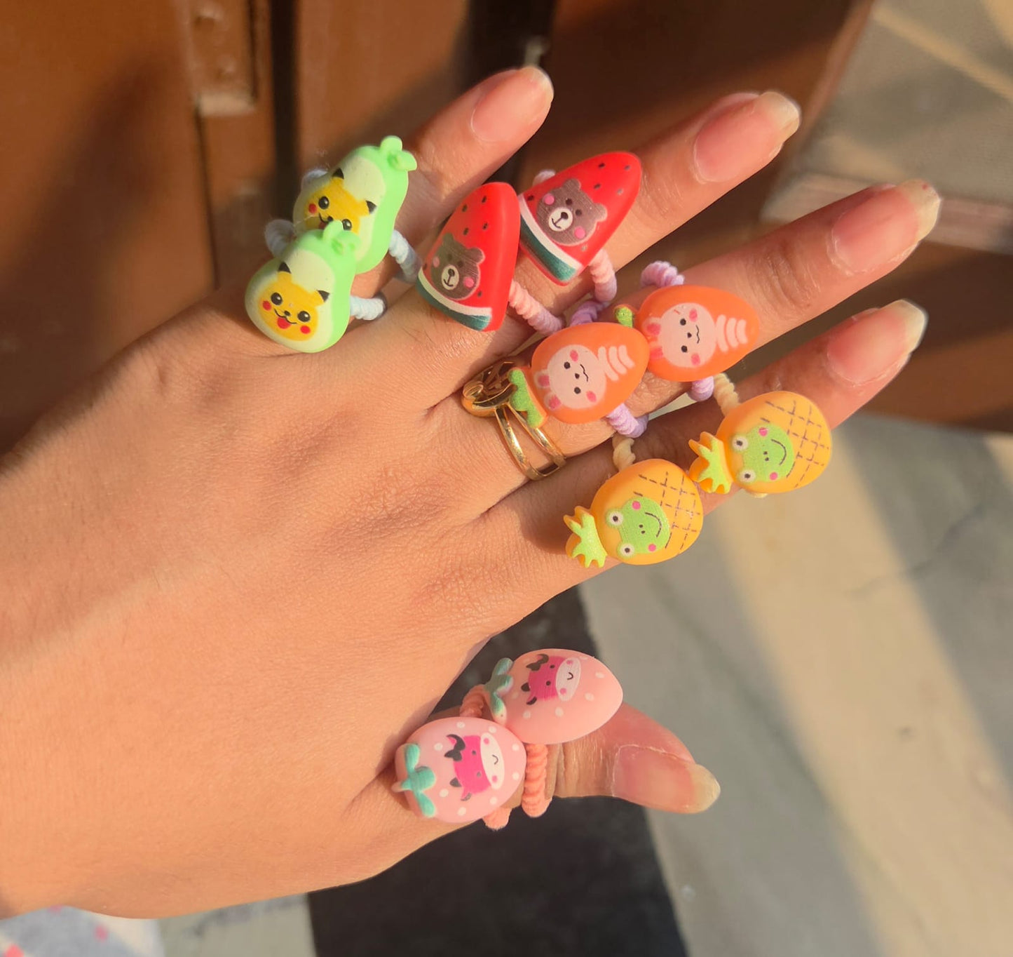 Close up of 5 pairs of matching toddler elastic hair bands featuring cute pineapple, avocado, strawberry, carrot, and watermelon designs.