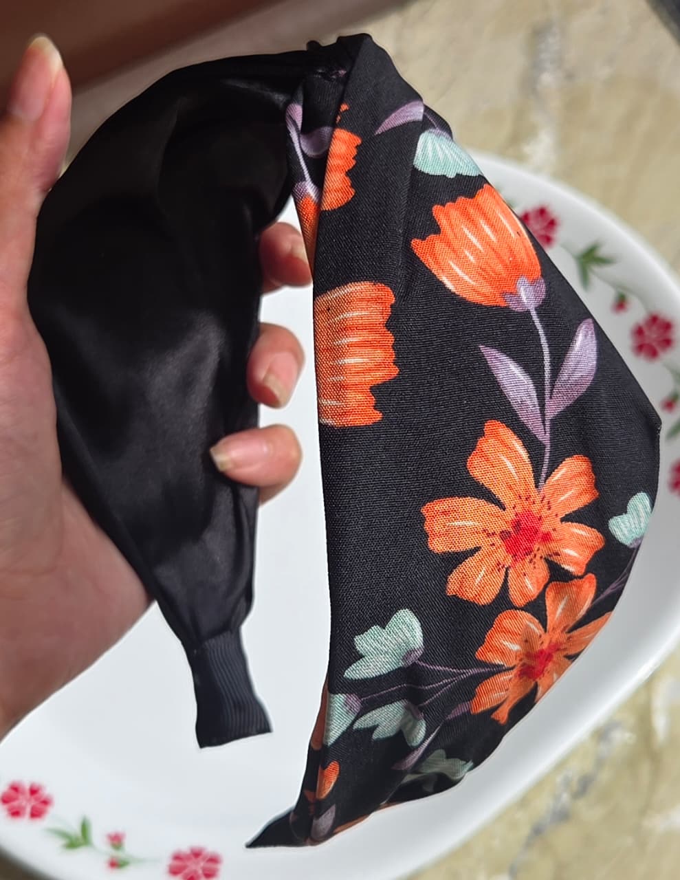    Black floral print satin twist headband with orange flower accents
