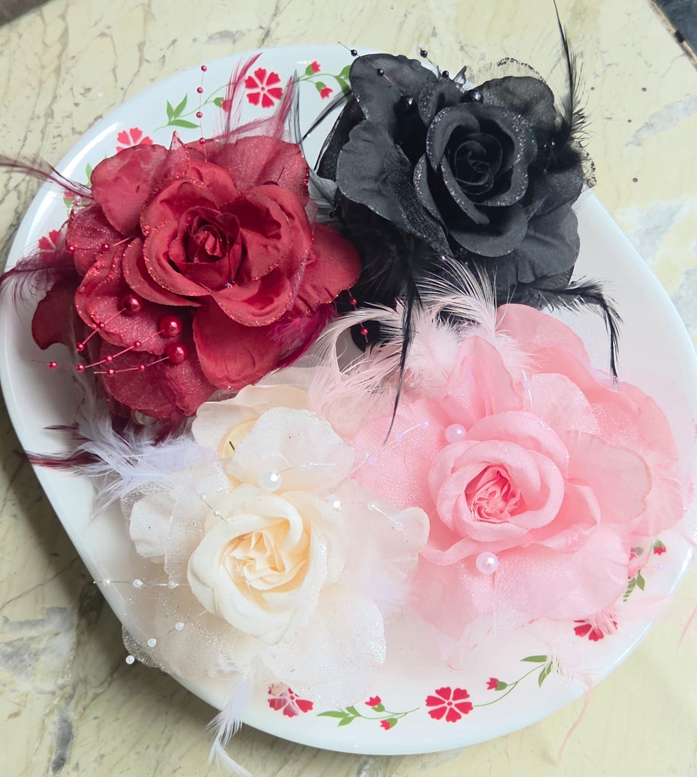    Group of four floral rose hair clutches with feathers and pearl accents in red, black, pink, and white.
