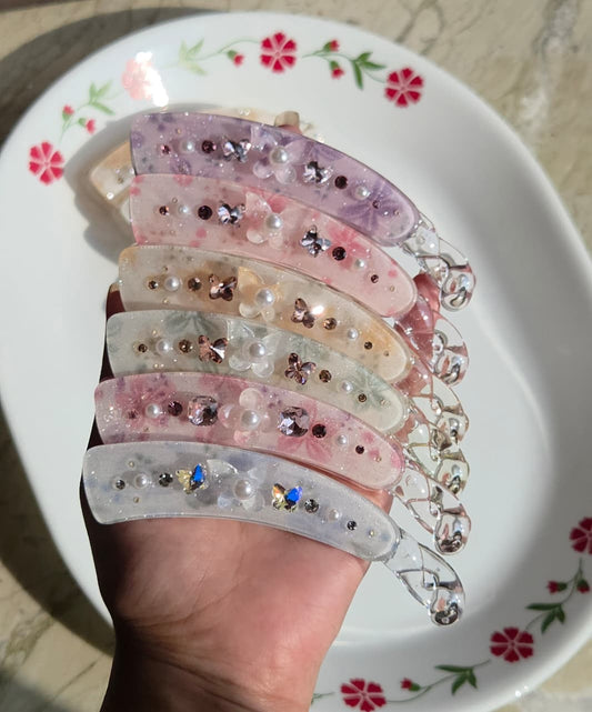    Six pastel floral banana hair clips with crystal butterfly and pearl embellishments held in hand
