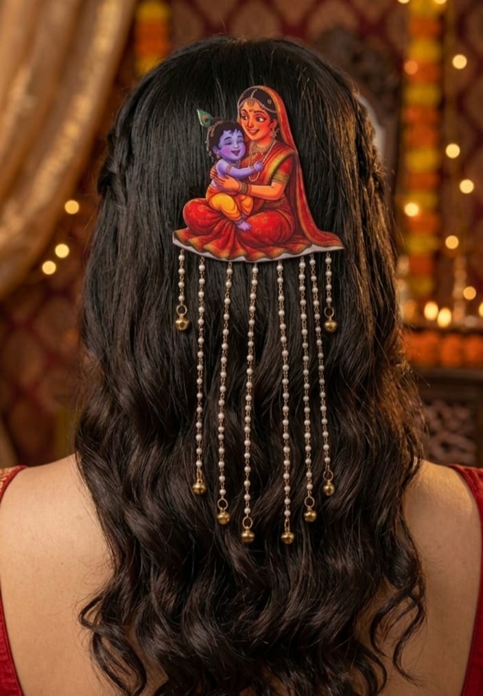 ​Rear view of a woman with long, wavy dark brown hair styled in a half-updo, showcasing a traditional Yashoda-Krishna hair accessory. The illustrated clip sits at the center, with seven long strands of white pearls and golden bells cascading down her hair against a warm, softly lit festive backdrop