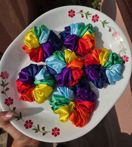 Vibrant handmade multi color rainbow satin scrunchie displayed on a white plate
