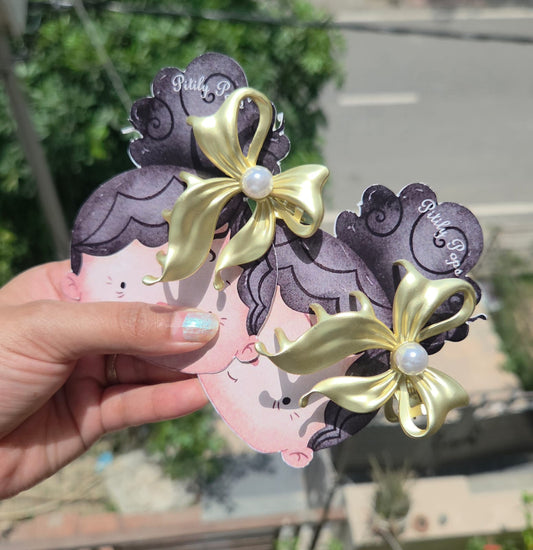 Premium gold-toned metallic claw clip in a fluid bow design held in hand, showcasing the glossy white pearl centerpiece.