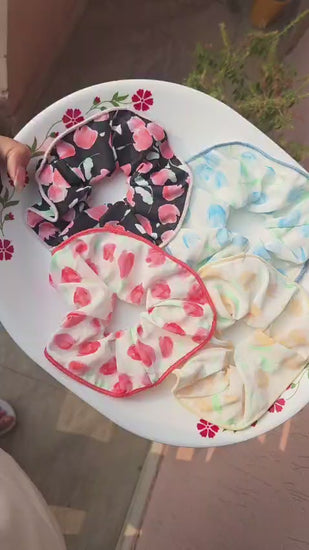 Pitily Pops handmade floral fabric scrunchies in four pastel color variants displayed on a white plate.