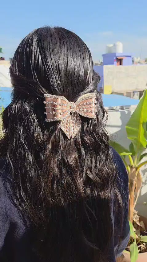 Rear view of a woman with long wavy dark brown hair styled with a sparkling champagne gold crystal hair bow barrette.