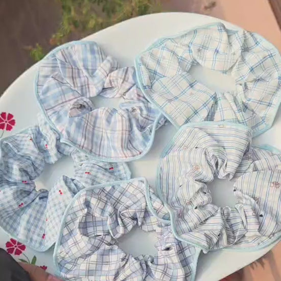 A collection of 5 aesthetic pastel blue and white plaid, gingham, and checkered cotton scrunchies displayed on a white plate.