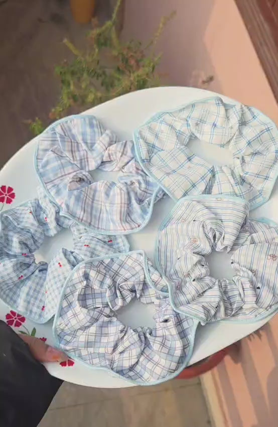A collection of 5 aesthetic pastel blue and white plaid, gingham, and checkered cotton scrunchies displayed on a white plate.